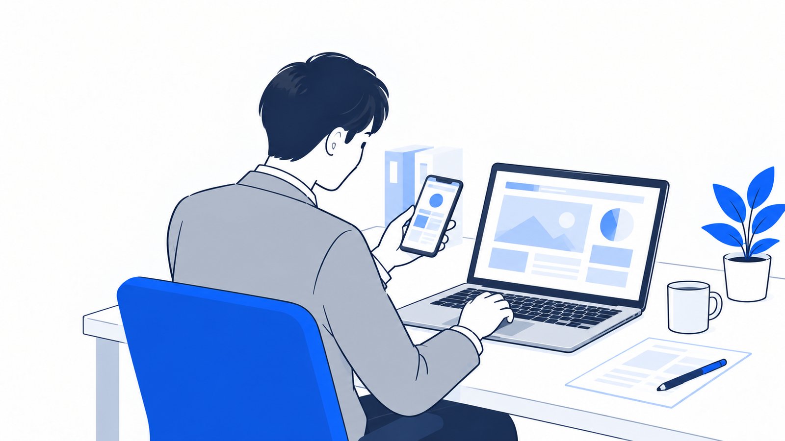 机の上のノートPCと、その横でスマホの画面を確認する会社員